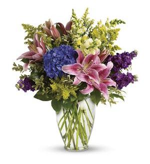 Bouquet of pink lilies, blue hydrangea, and purple flowers in a glass vase