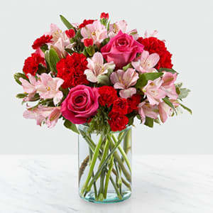 Bouquet of pink roses, red carnations, and pale pink alstroemeria in a glass vase