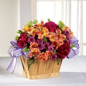 Mixed orange, purple, and red flowers in a wooden basket with a purple ribbon