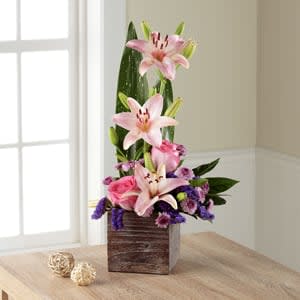 Pink lilies and mixed purple flowers in a wooden cube vase