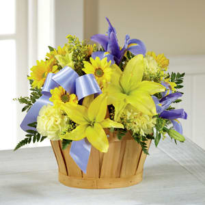 Yellow lilies and purple flowers in a wooden basket with a blue ribbon