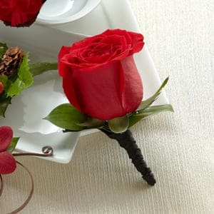 Red rose boutonniere with green leaves on a white tray