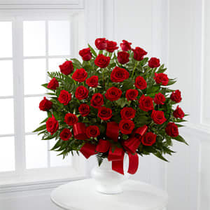 Red roses arranged in a white vase with a red ribbon