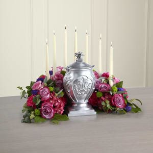 Pink and purple floral arrangement around a silver urn with tall white candles