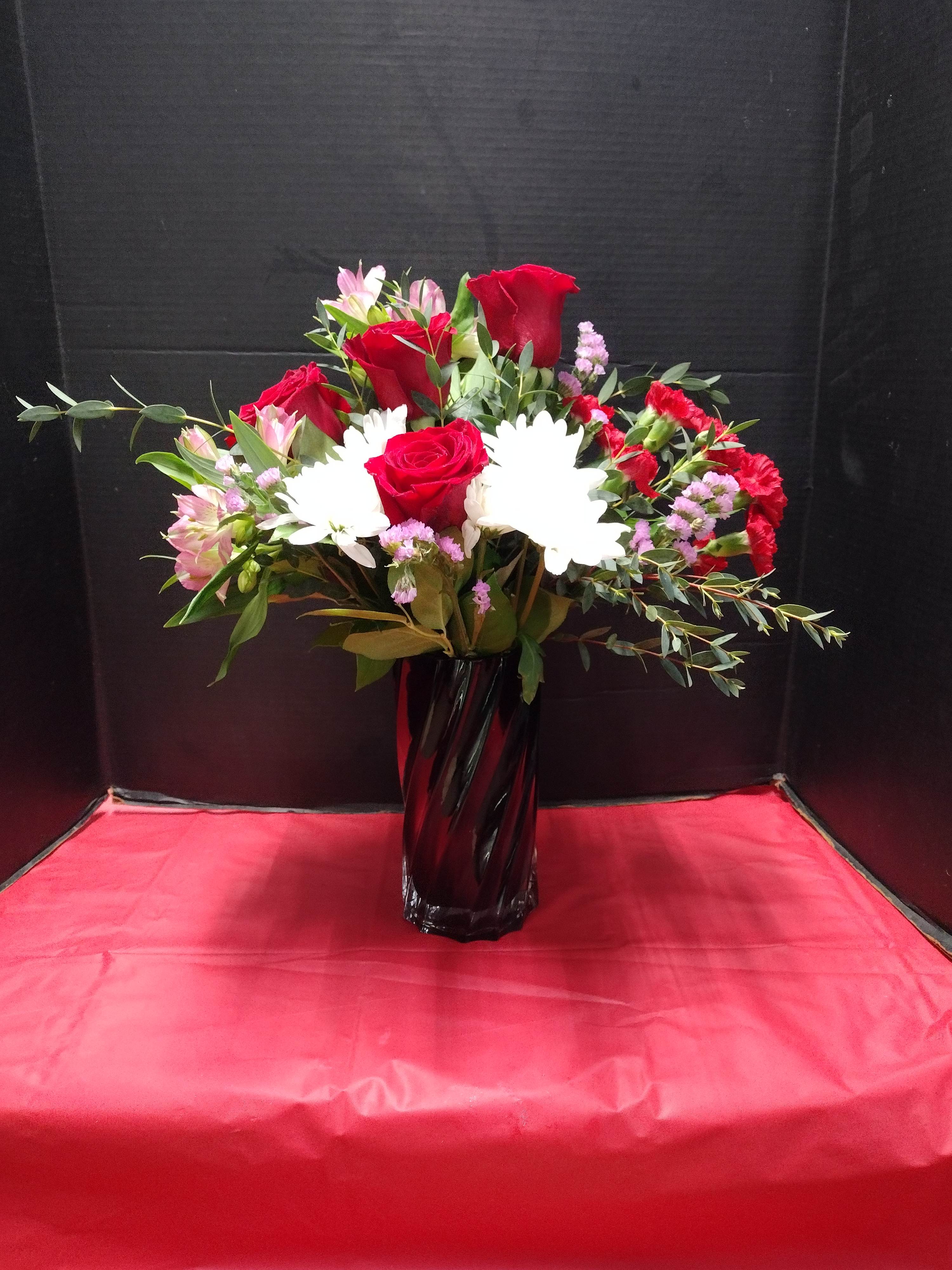Red roses and white daisies arranged in a tall black vase