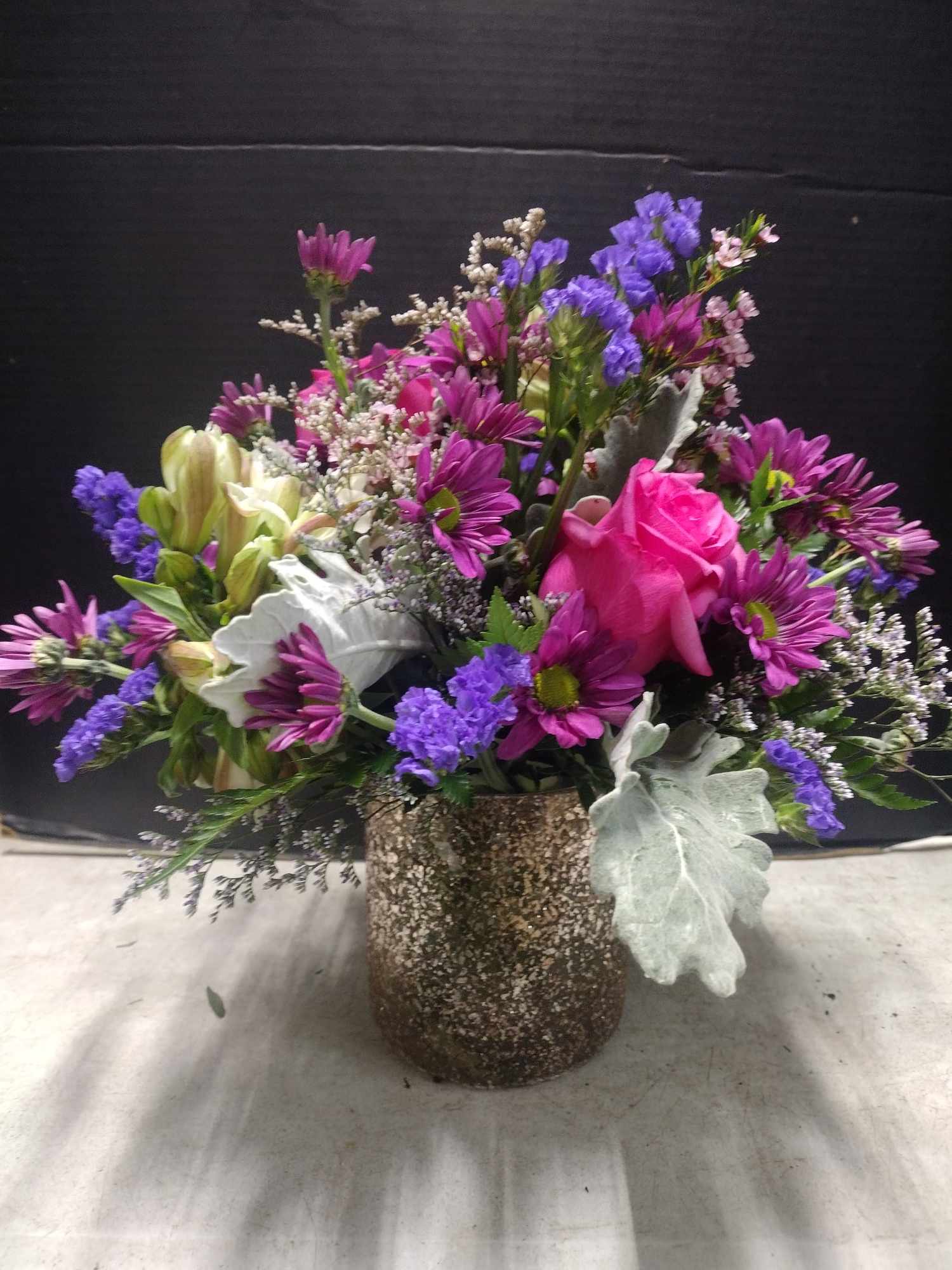 Mixed bouquet with pink rose, purple daisies, and a speckled vase