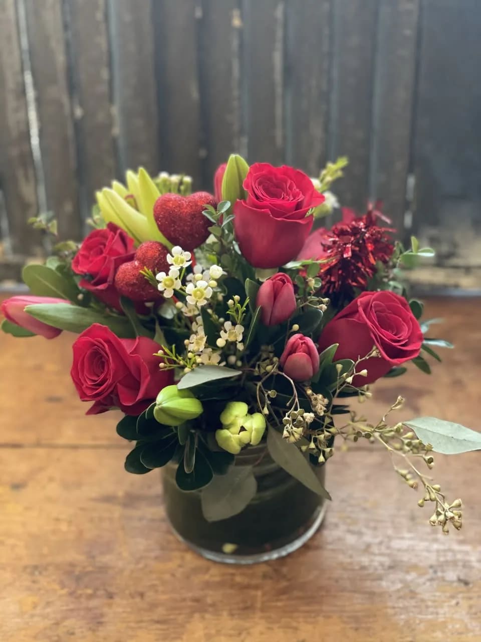 Red roses and tulips arranged in a glass vase with small white filler flowers