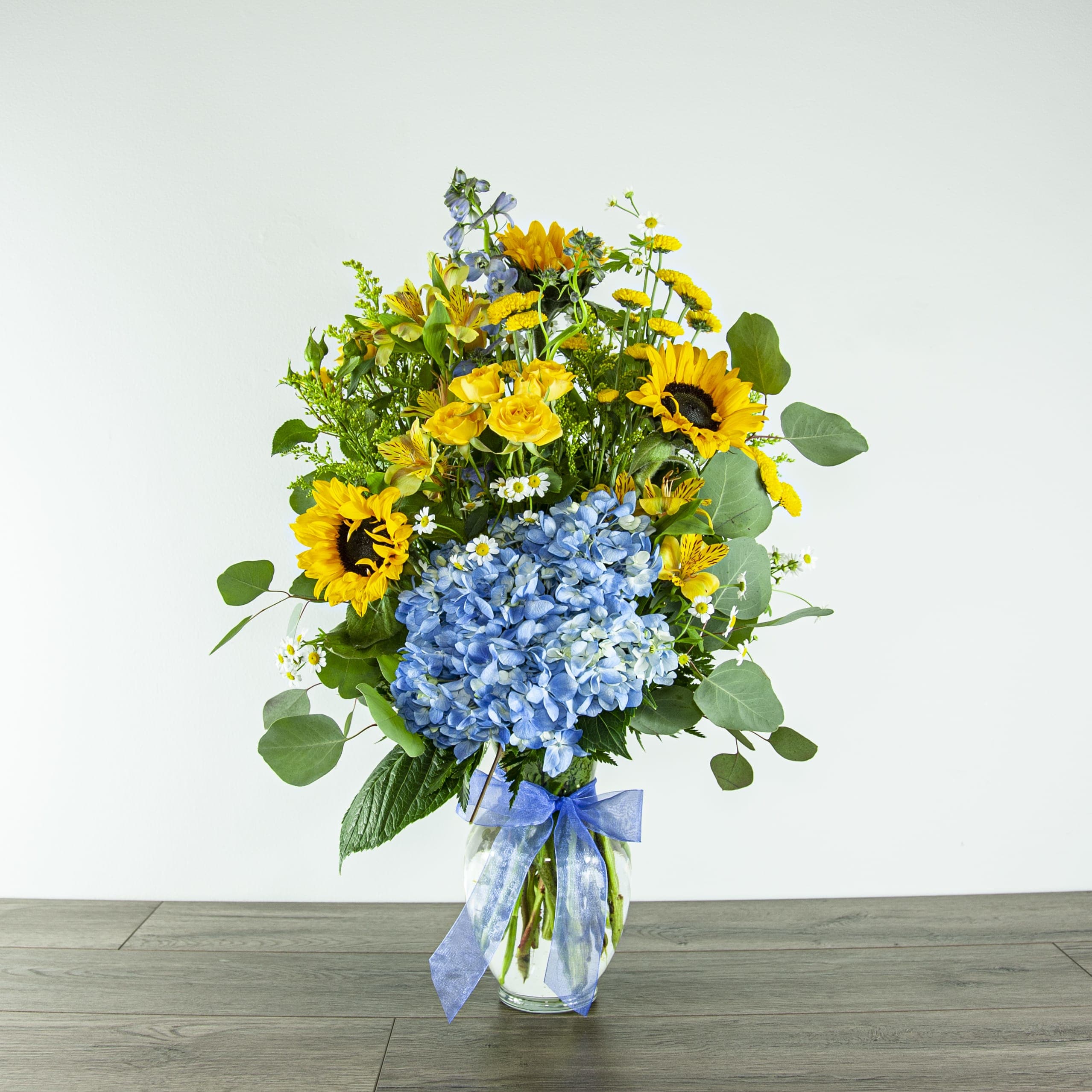 Bouquet of sunflowers, blue hydrangea, and yellow blooms in a glass vase