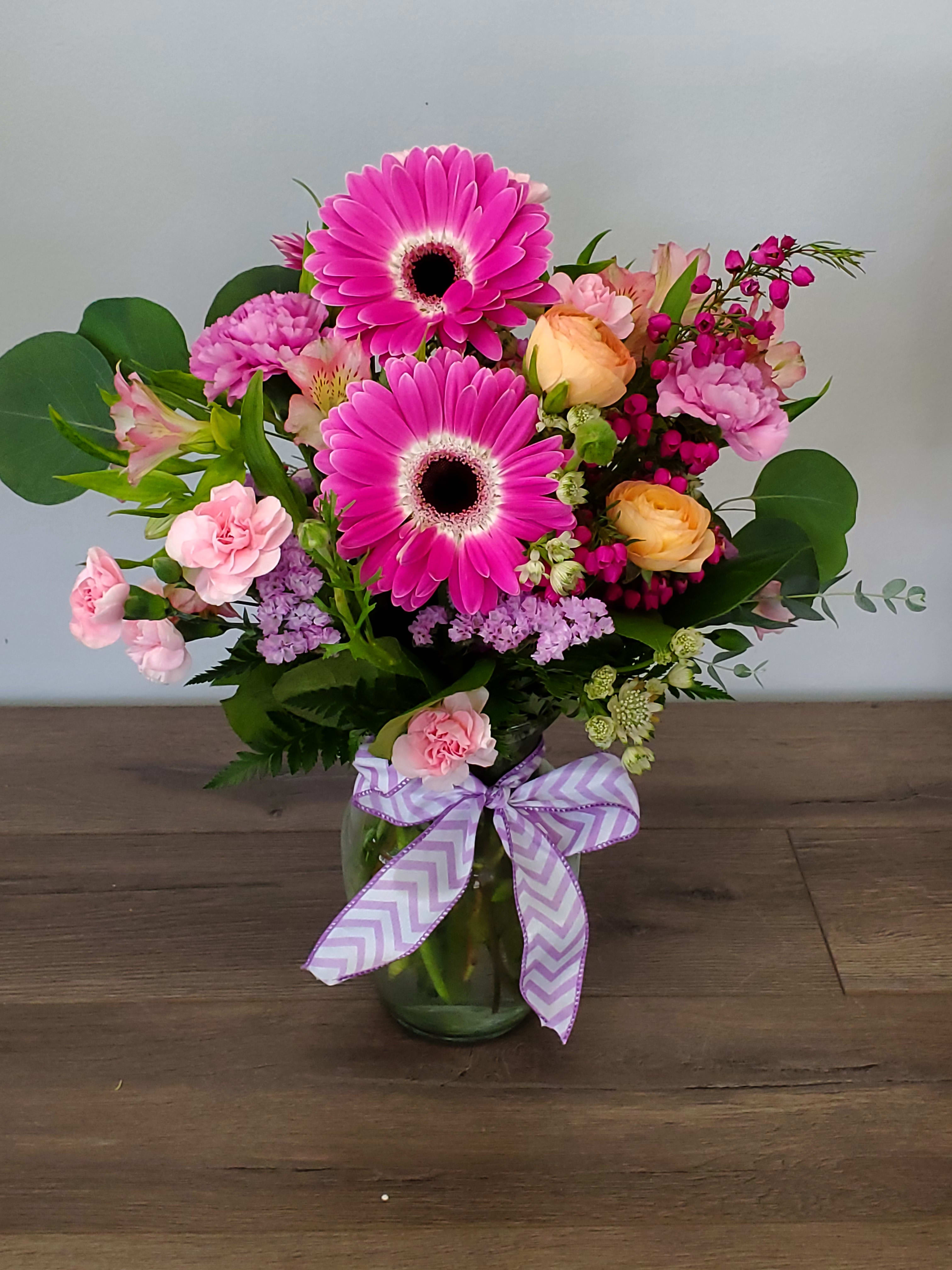 Pink gerbera and mixed flowers in a glass vase with a lavender ribbon