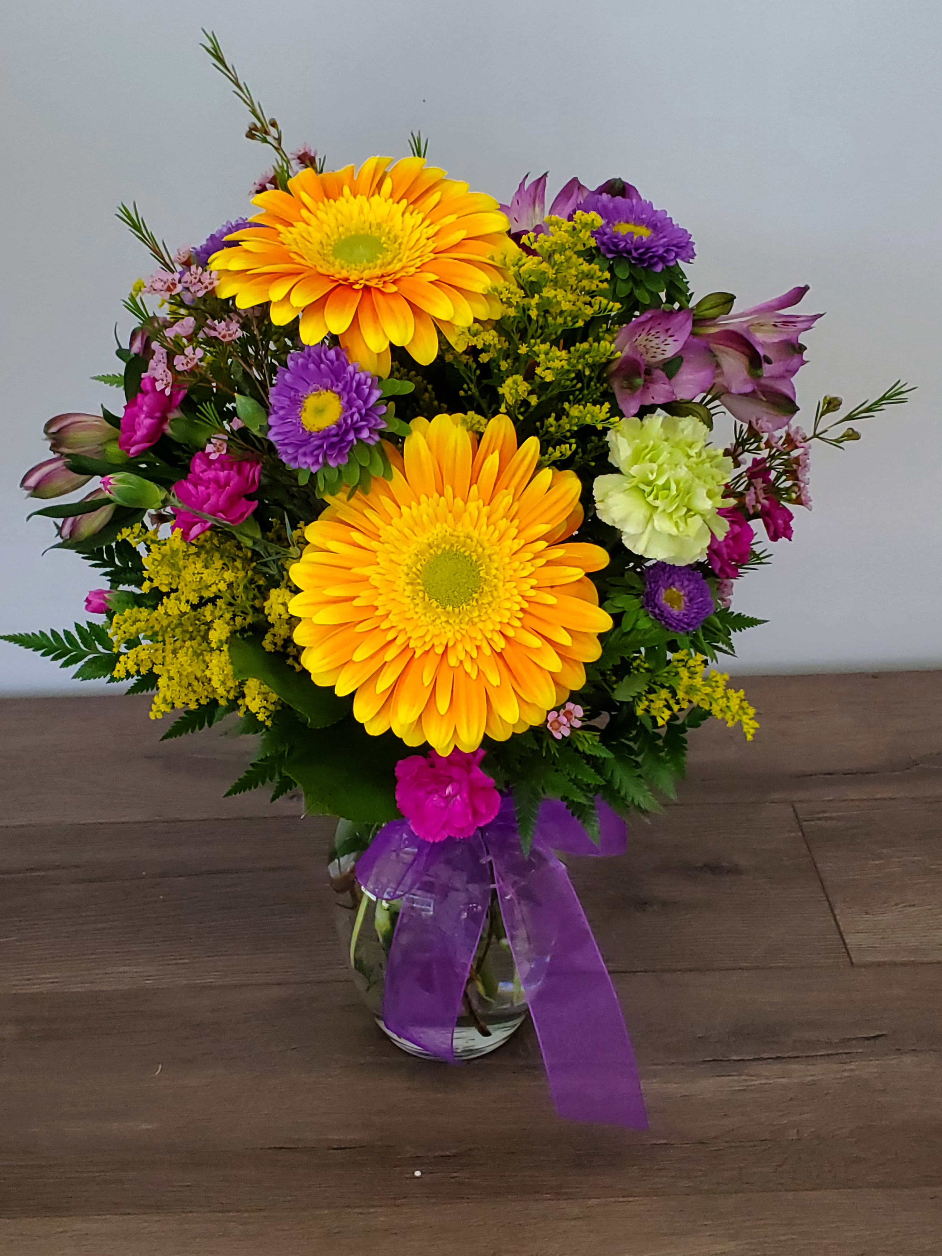 Mixed bouquet of yellow gerbera daisies and purple flowers in a glass vase