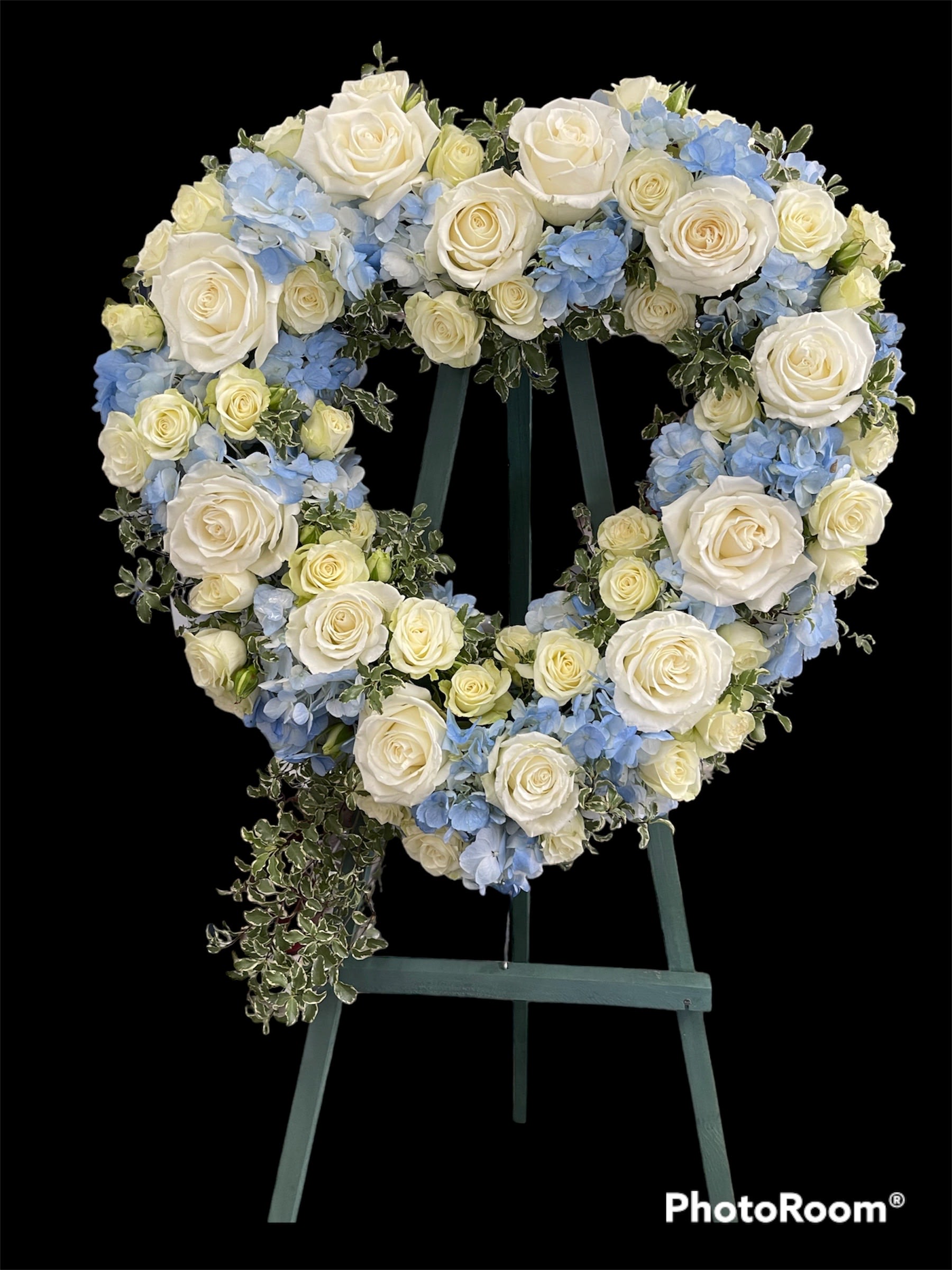 Heart-shaped floral wreath of white roses and blue hydrangeas on an easel