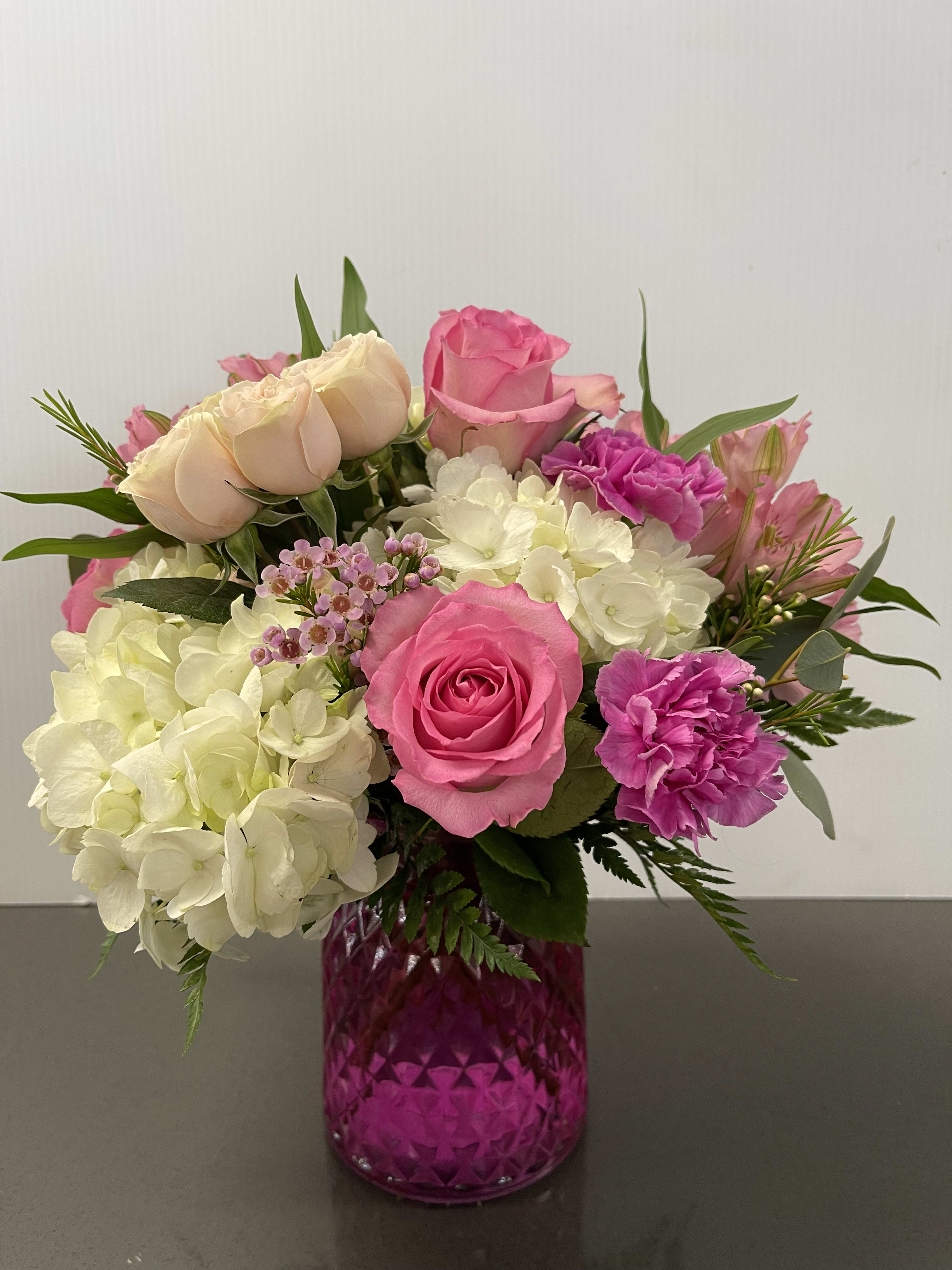 Pink and white flower arrangement in a magenta glass vase