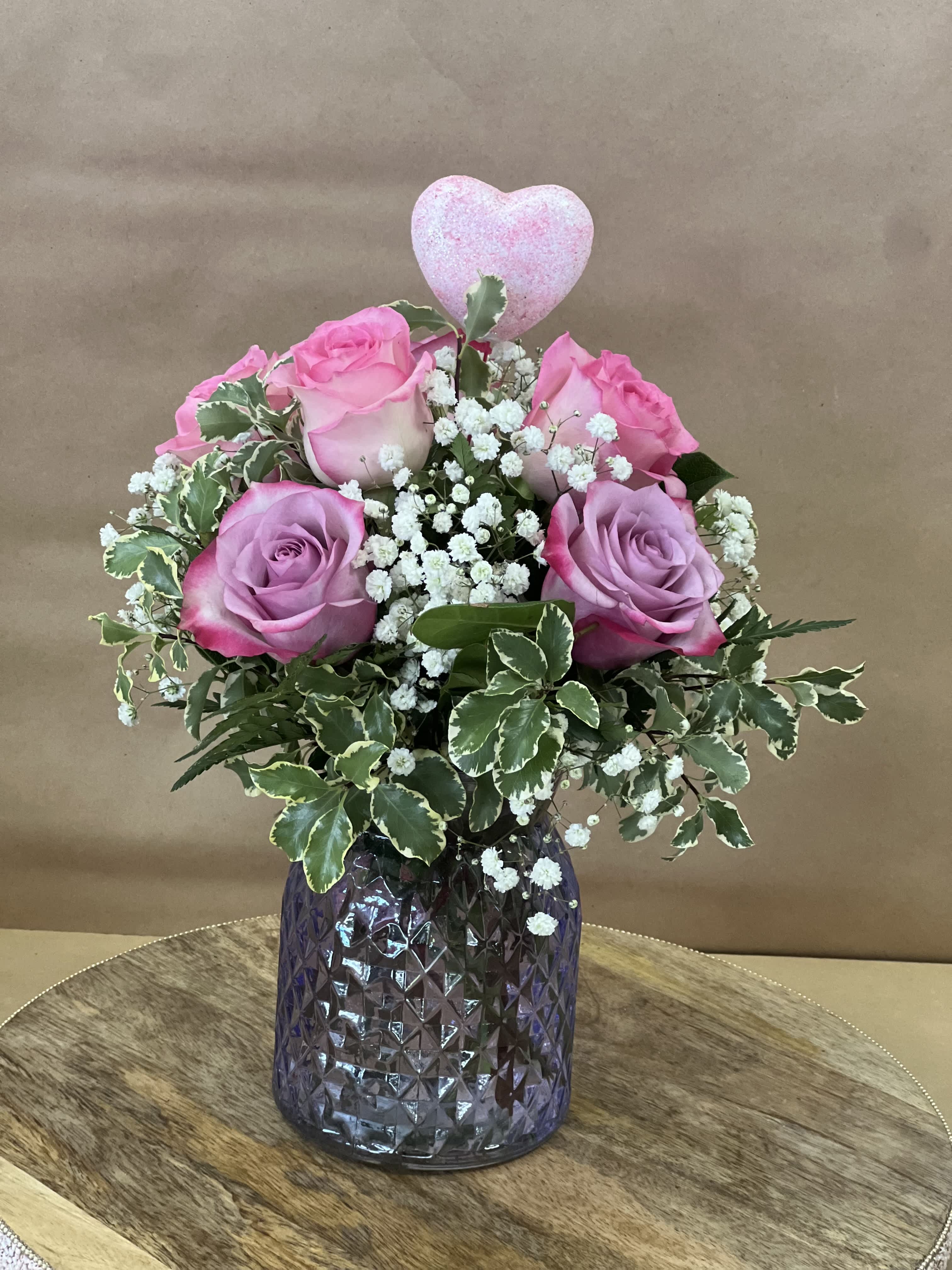 Pink roses with baby's breath in a purple glass vase, topped with a heart pick