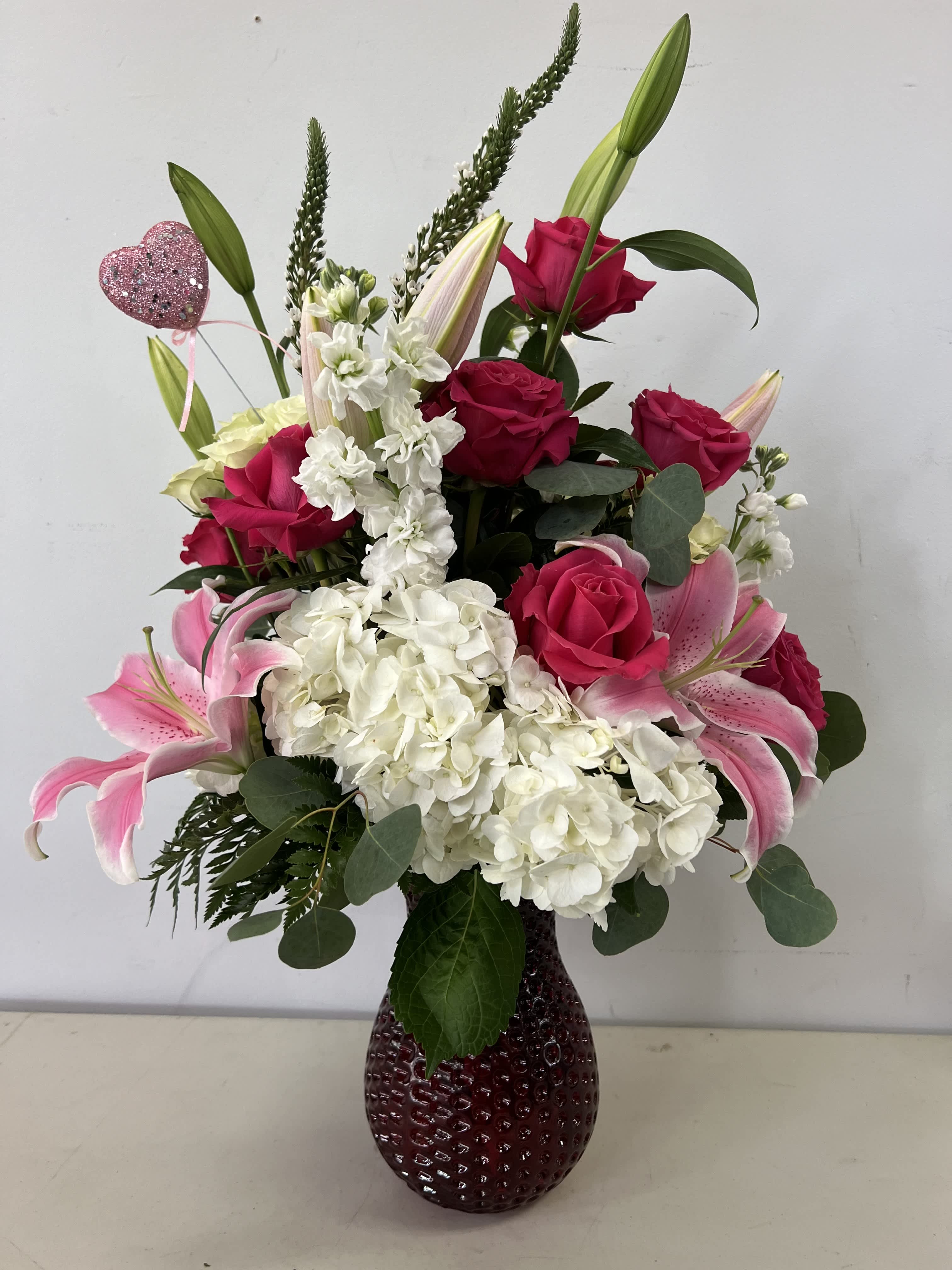 Pink roses and lilies arranged in a dark glass vase with white hydrangeas.