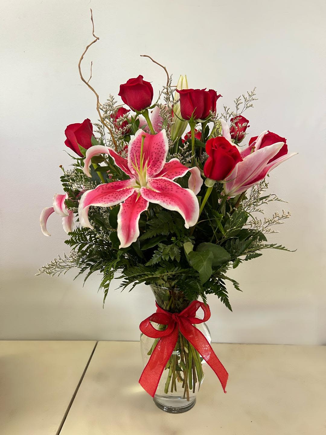 Red roses and pink lilies in a glass vase with a red ribbon