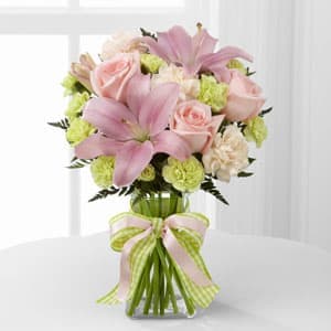 Pink lilies and roses in a glass vase with a ribbon bow