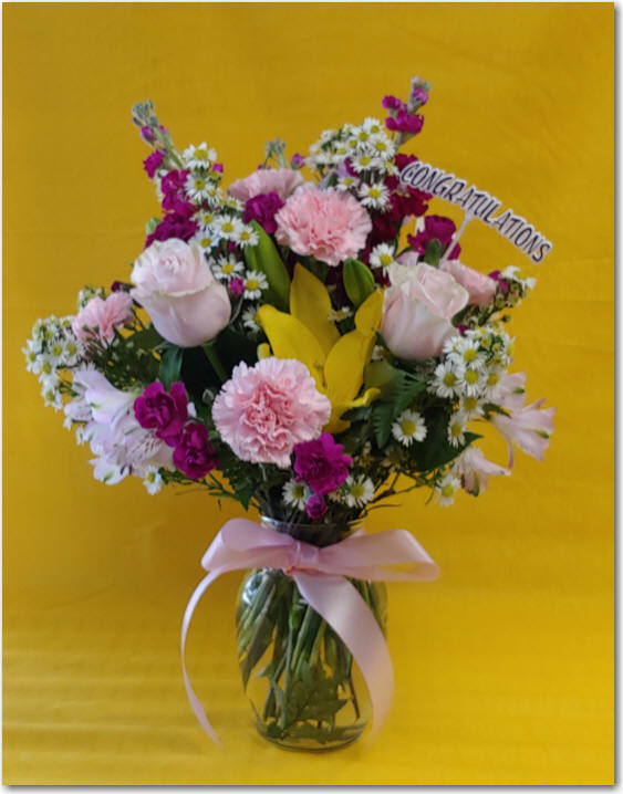 Mixed pink and white flowers in a glass vase with a congratulations sign