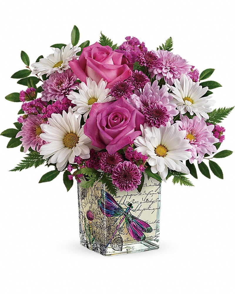 Teleflora's Wildflower In Flight Bouquet - Reminiscent of a love letter written in a Parisian garden, this whimsical cube vase will make mom's heart soar, especially when delivered for Mother's Day with a cheerful roses and daisies bouquet! This bright bouquet includes hot pink roses, purple button spray chrysanthemums, lavender cushion spray chrysanthemums, white daisy spray chrysanthemums, raspberry sinuata statice, leatherleaf fern, and huckleberry. Delivered in a Wildflower In Flight cube. (z)