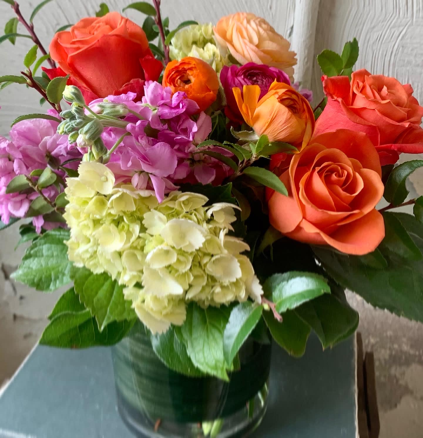 Mixed bouquet of orange roses, hydrangeas, and pink flowers in a glass vase