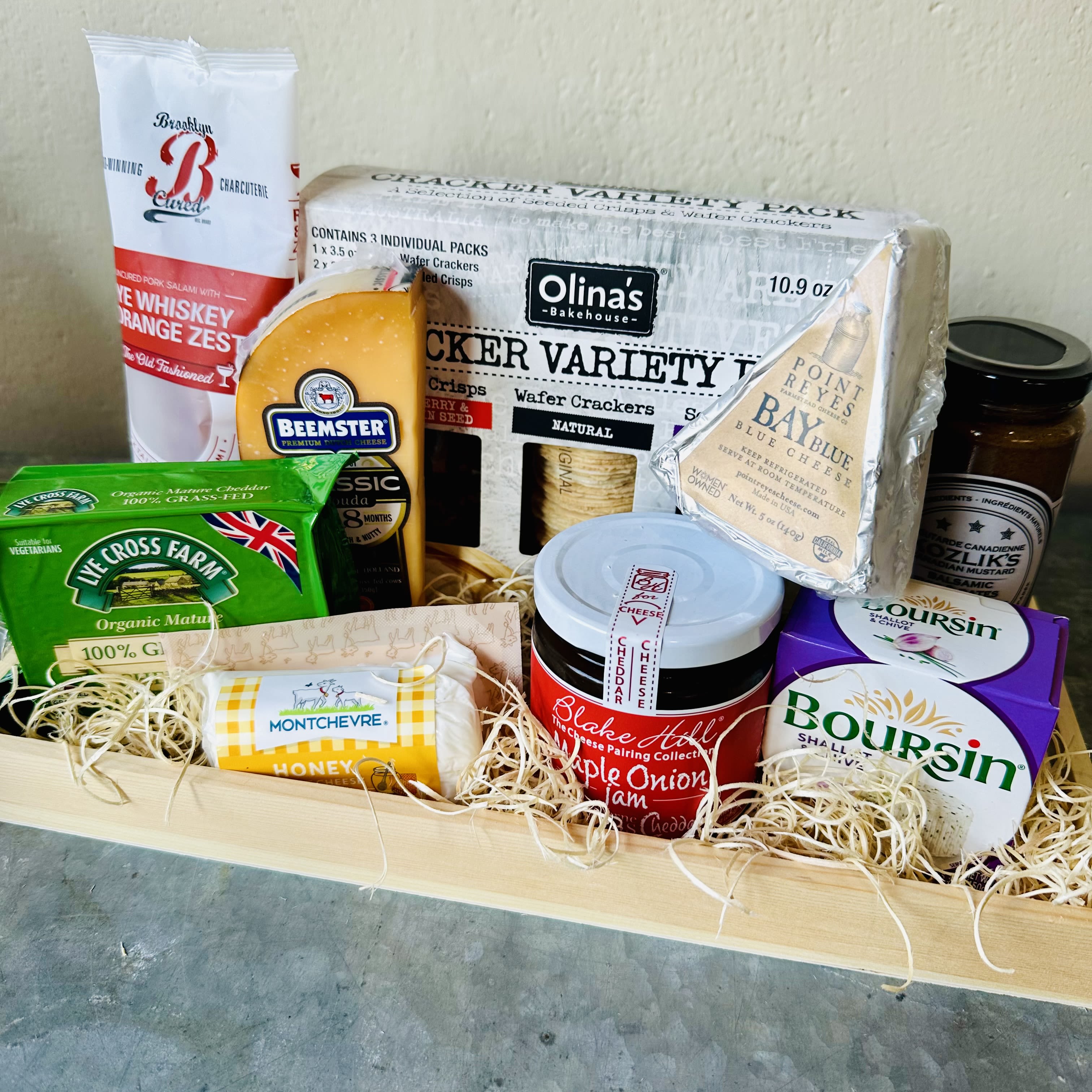 Assorted cheeses, crackers, salami, and jam in a wooden gift tray