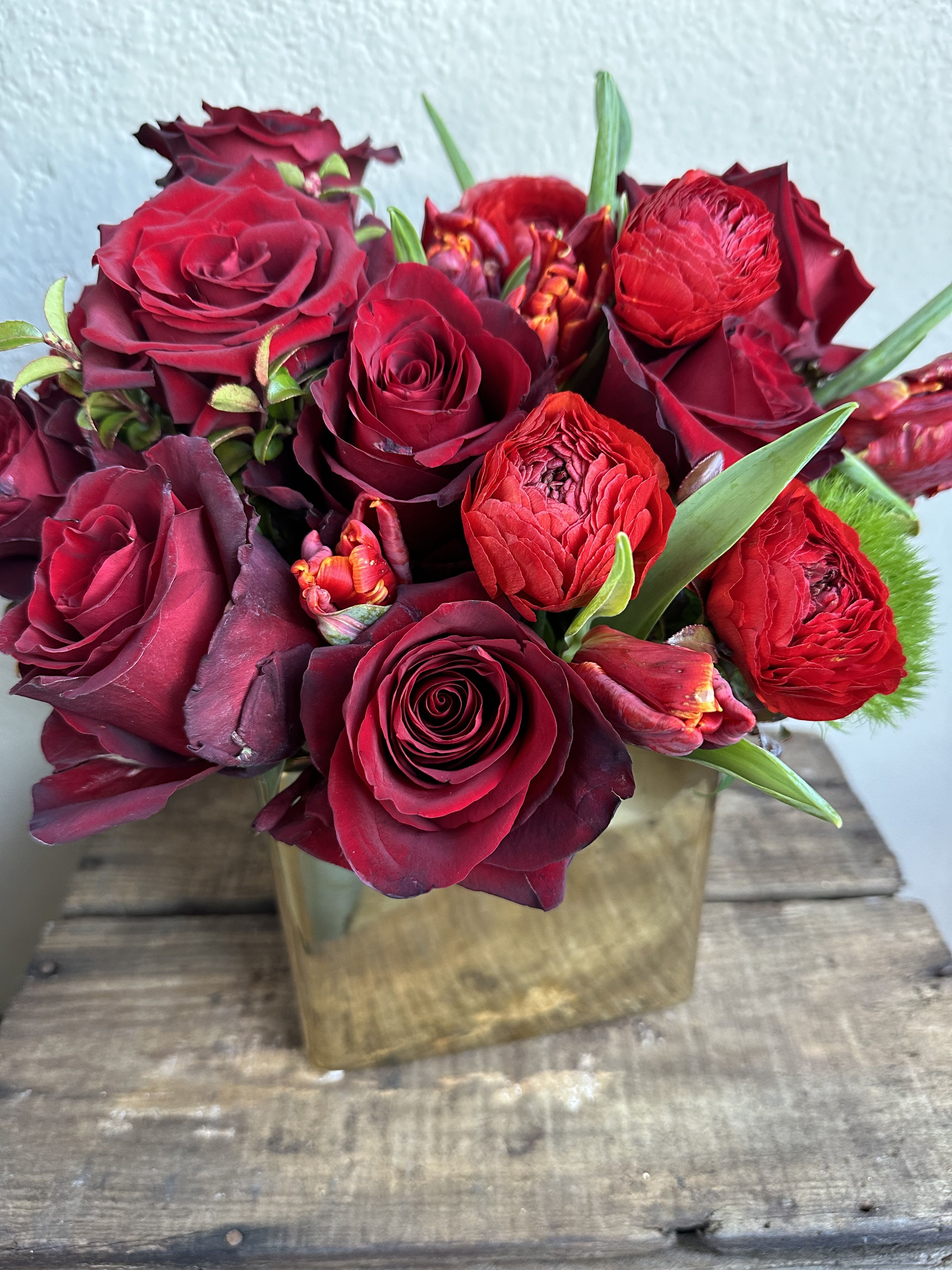 Red roses and ranunculus arranged in a square gold vase