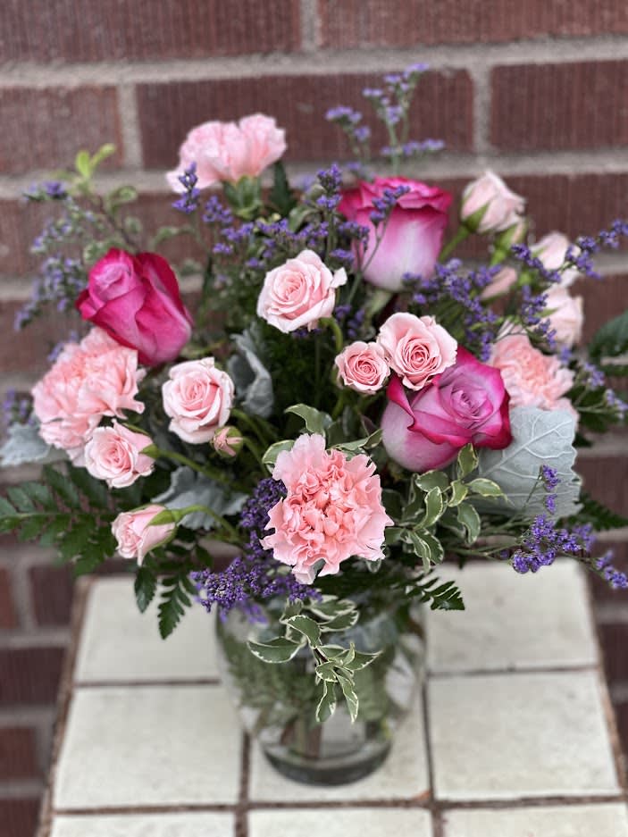 Pink roses and carnations arranged in a glass vase with purple filler flowers.