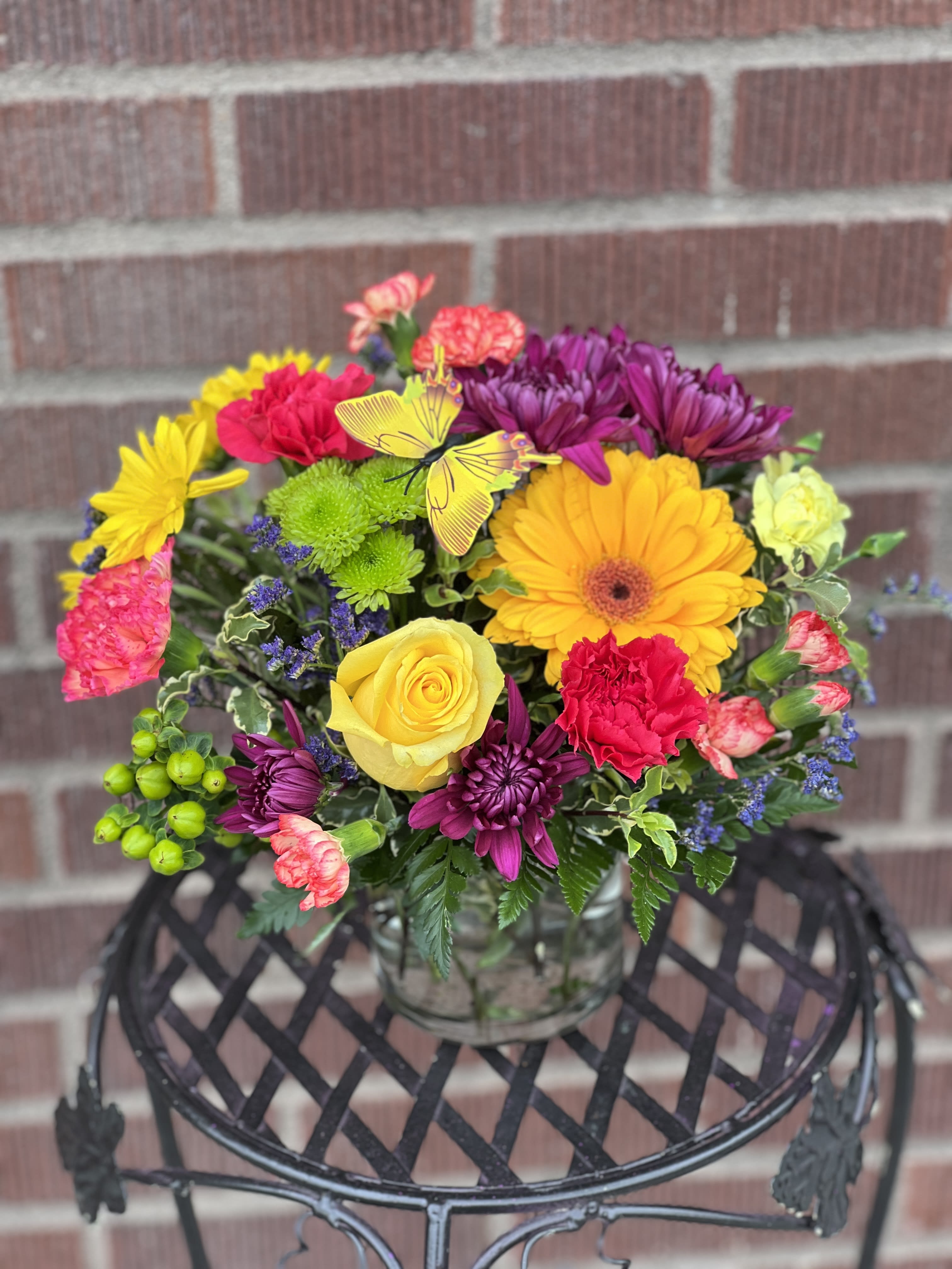 Colorful mixed bouquet in a clear glass vase with a butterfly pick