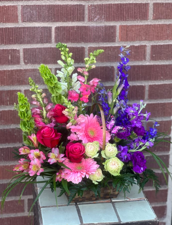 Basket arrangement of pink, purple, and red flowers with a butterfly pick