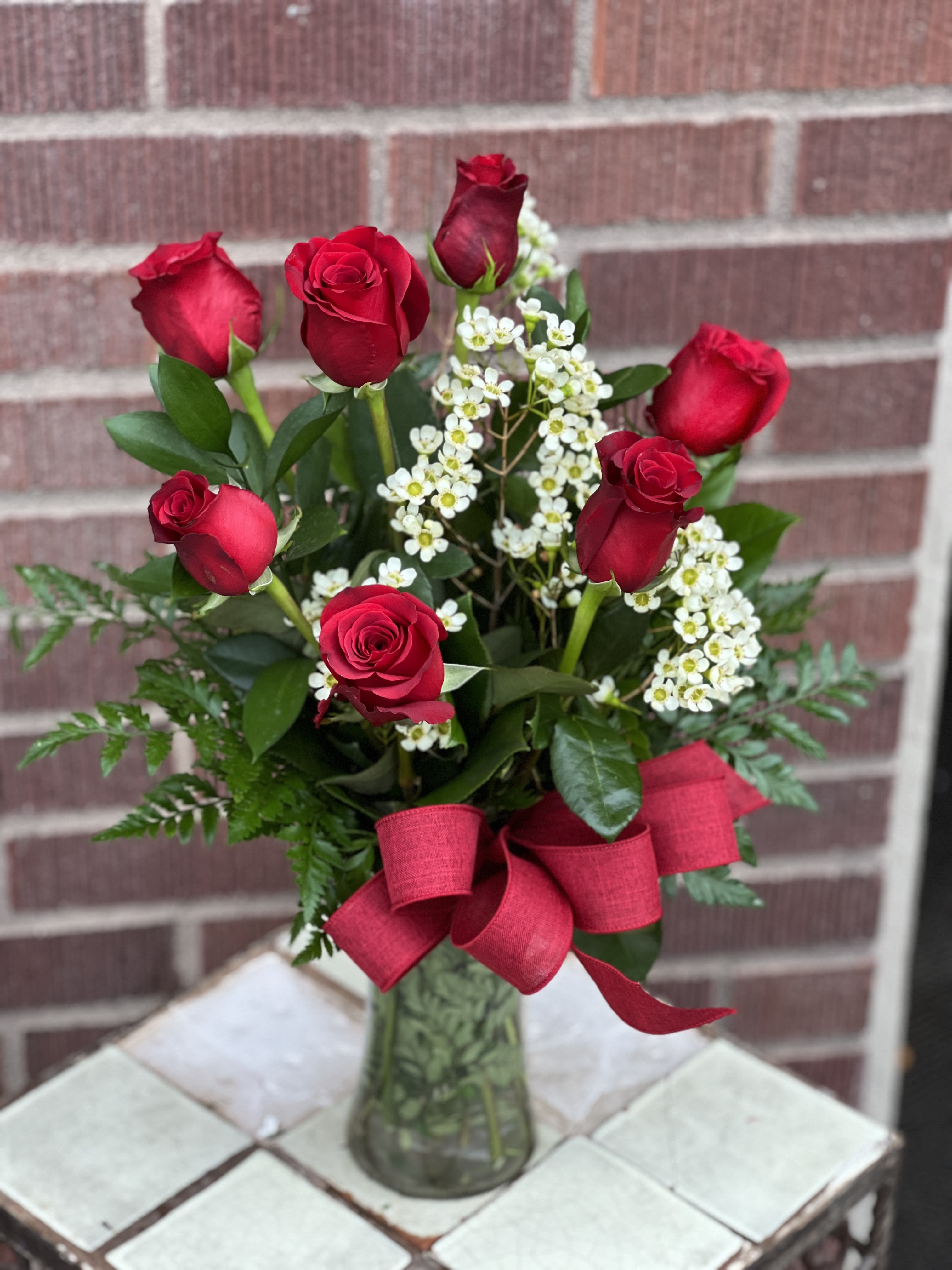 Red roses with white filler flowers in a glass vase and red ribbon