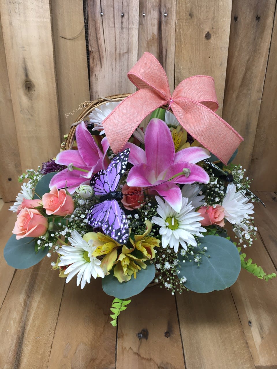 Basket arrangement with pink lilies, white daisies, and a pink bow