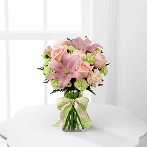 Pink lilies and roses in a glass vase with a ribbon bow