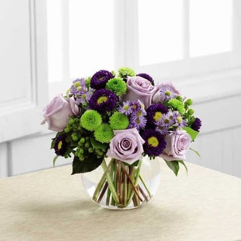 Lavender roses and purple-green pompom flowers in a clear glass vase