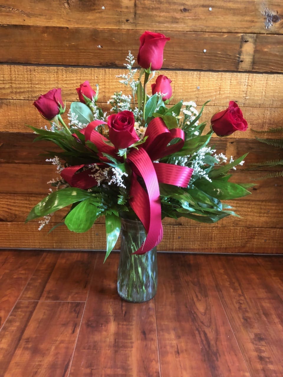 Red roses arranged in a clear glass vase with a pink ribbon
