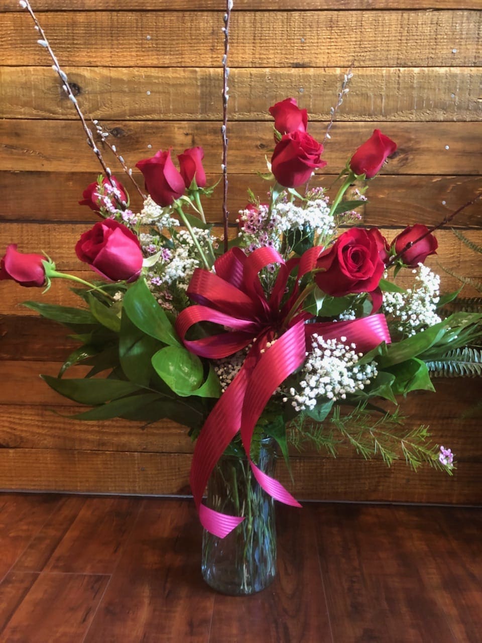 Red roses arranged in a glass vase with a pink ribbon