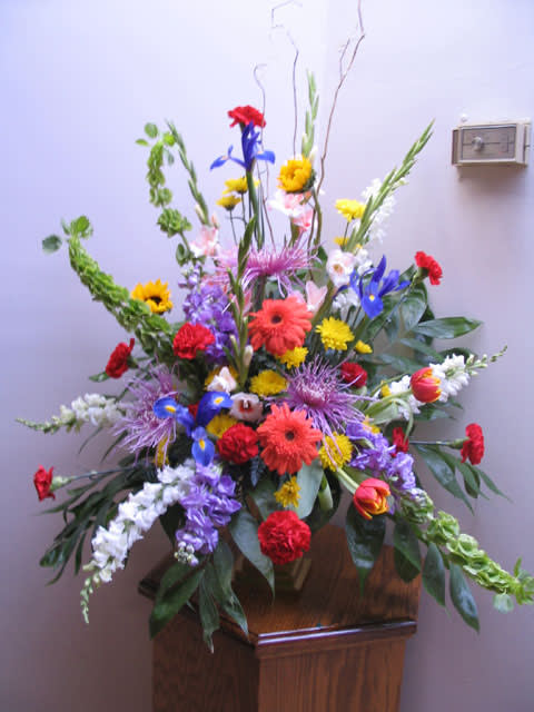 Tall mixed flower arrangement with bright red, yellow, blue, and purple blooms