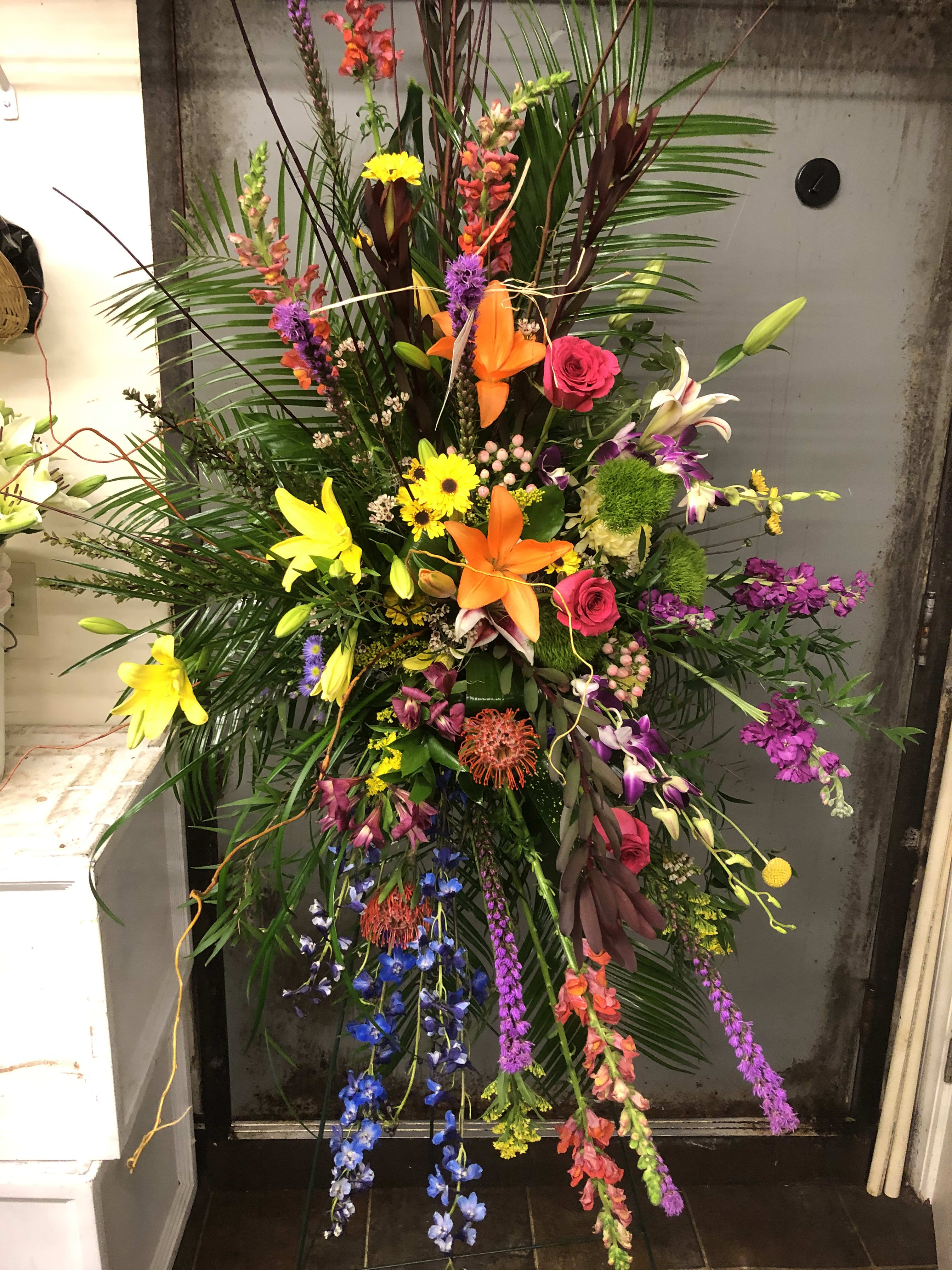 Tall tropical floral spray with lilies, roses, and orchids