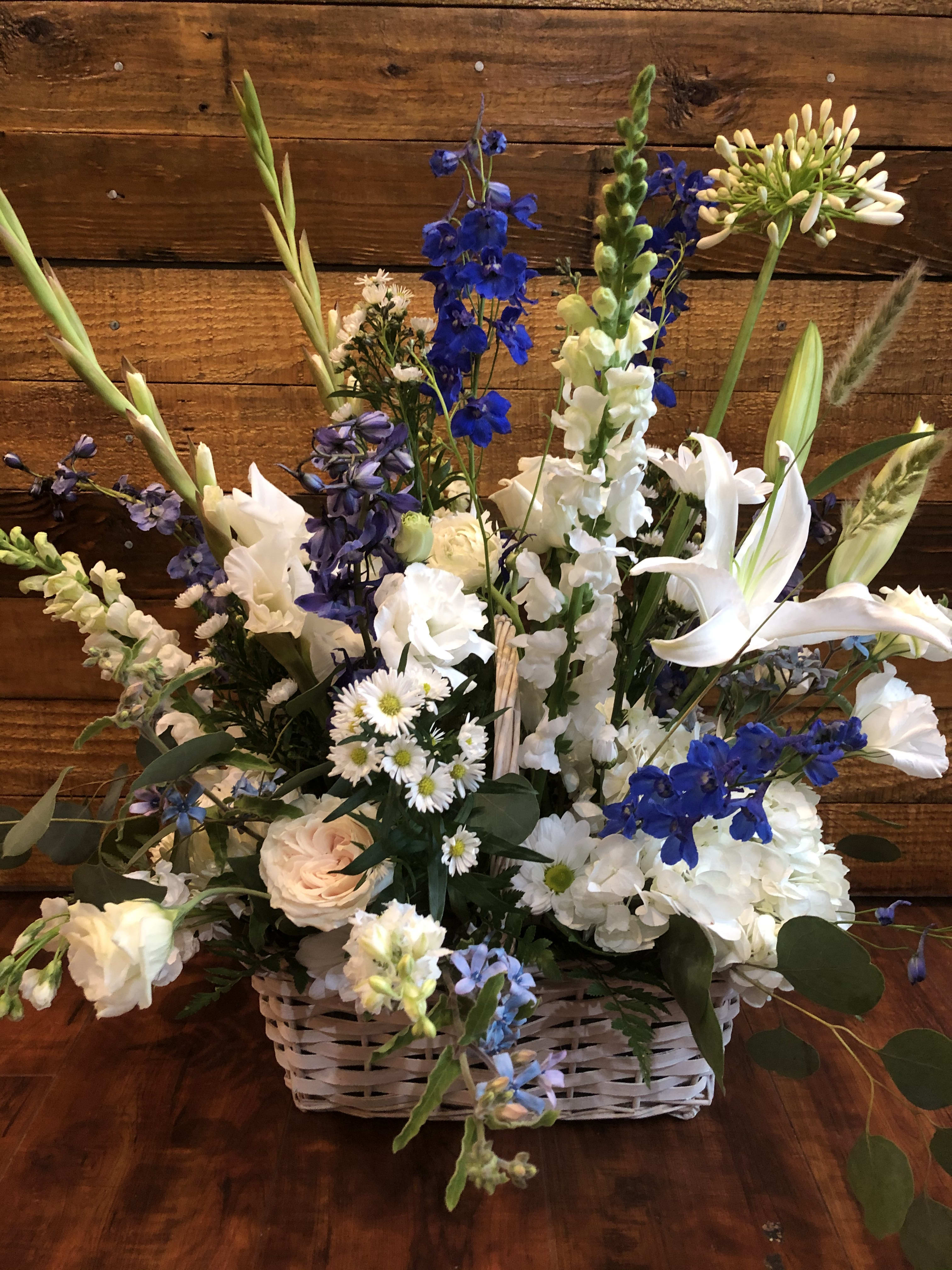 Tall white and blue flower basket with lilies, roses, daisies, hydrangeas, and delphinium in a white woven basket