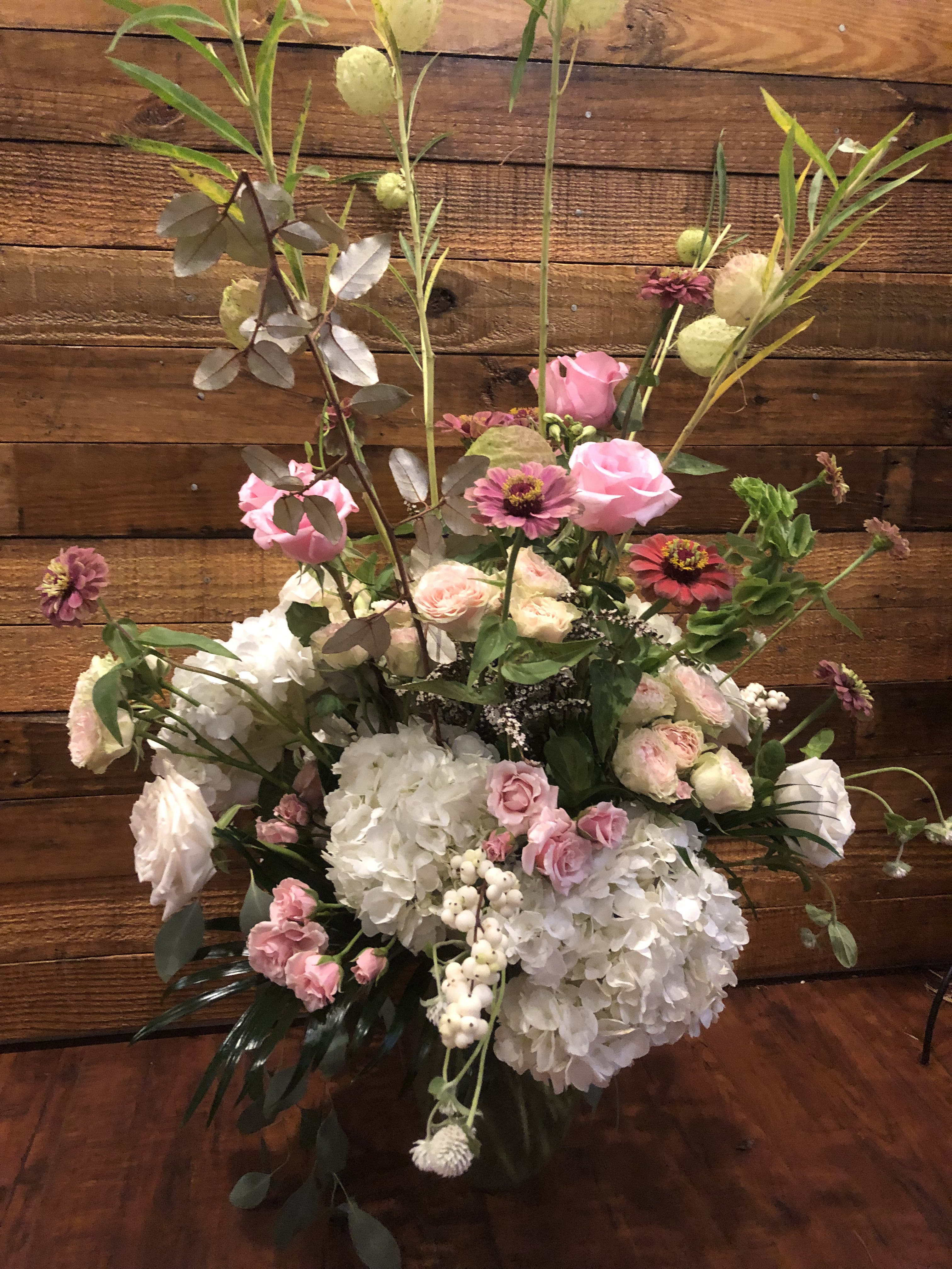 Tall floral arrangement with pink roses, white hydrangeas, and mixed blooms