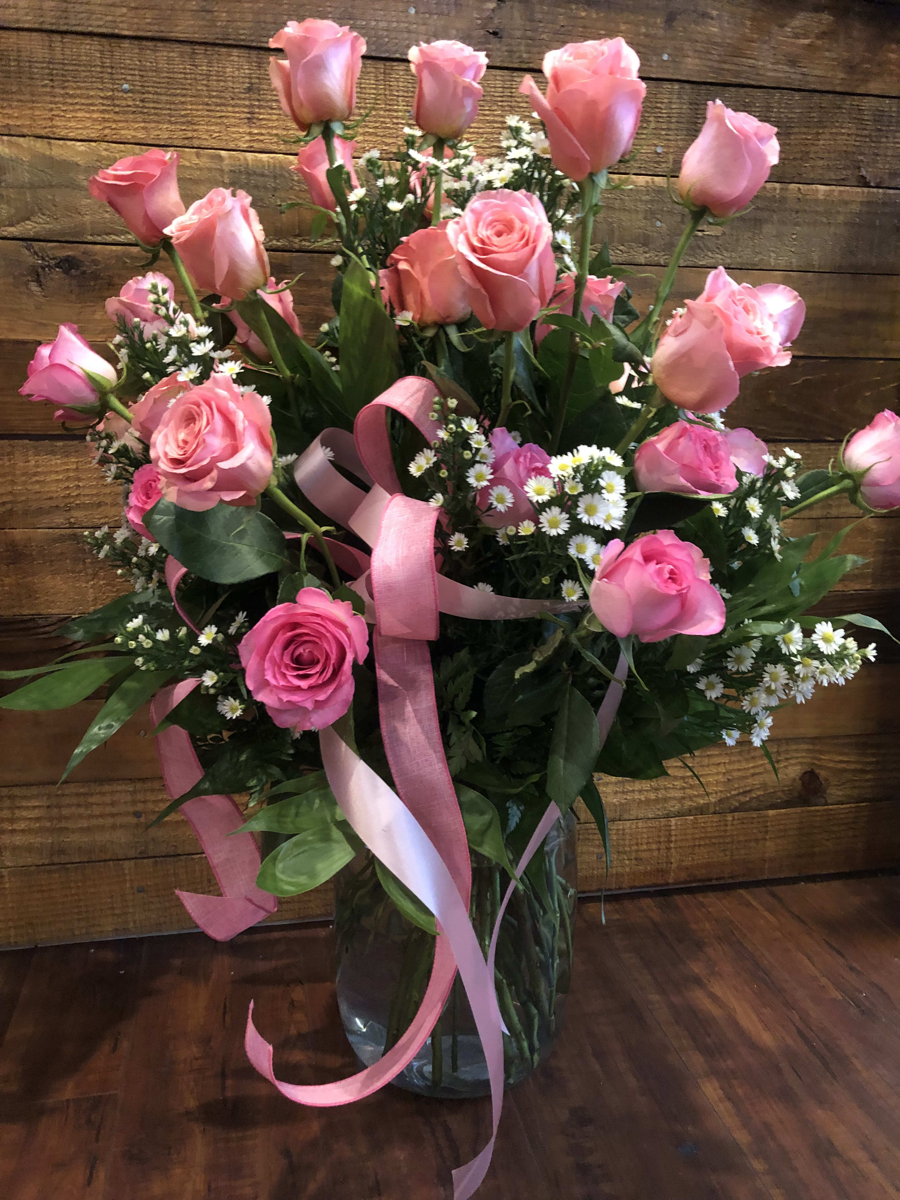 Pink roses and small white daisies in a glass vase with pink ribbon