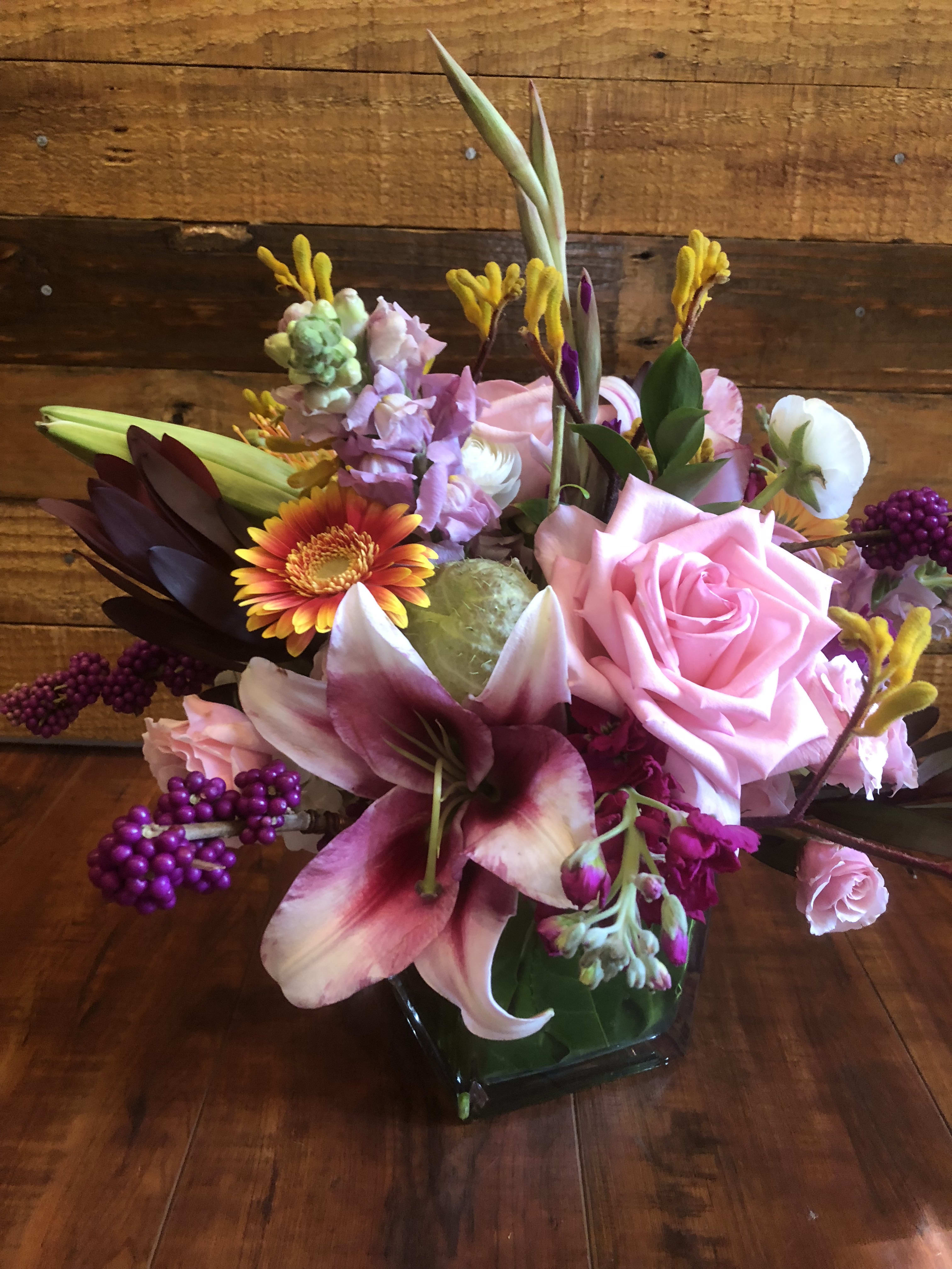 Pink roses and lilies in a glass vase with purple accents