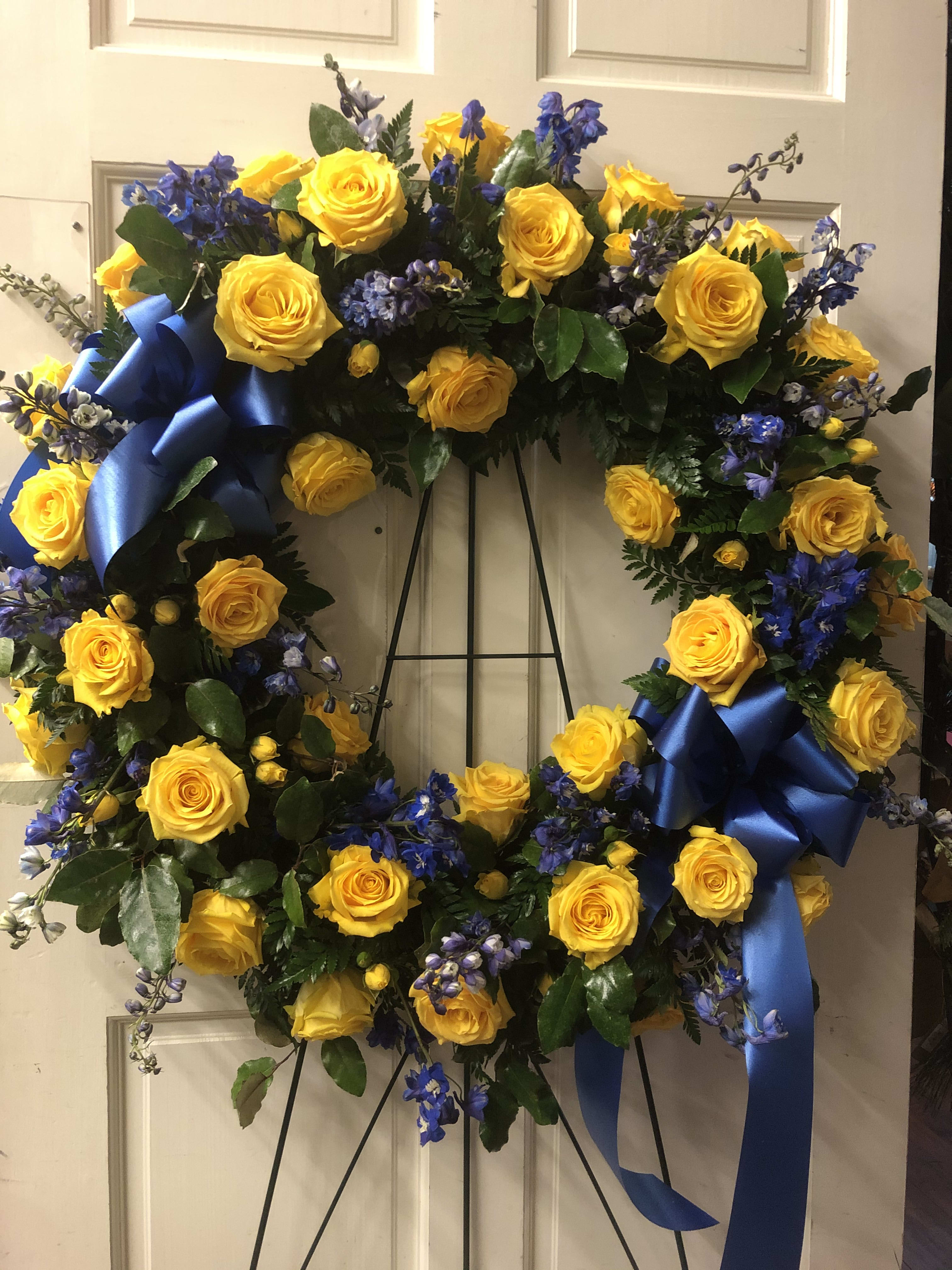 Yellow rose wreath with blue ribbon accents on a stand