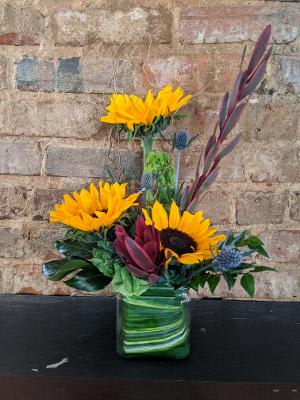 Sunflower arrangement in a green glass vase with burgundy foliage