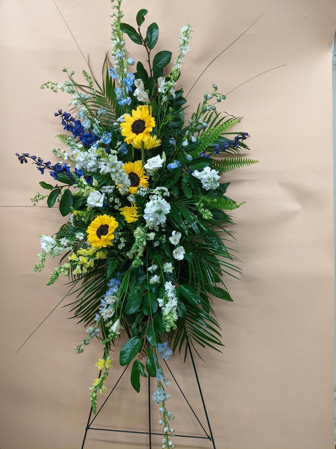 Standing floral spray with sunflowers, blue and white flowers, and greenery