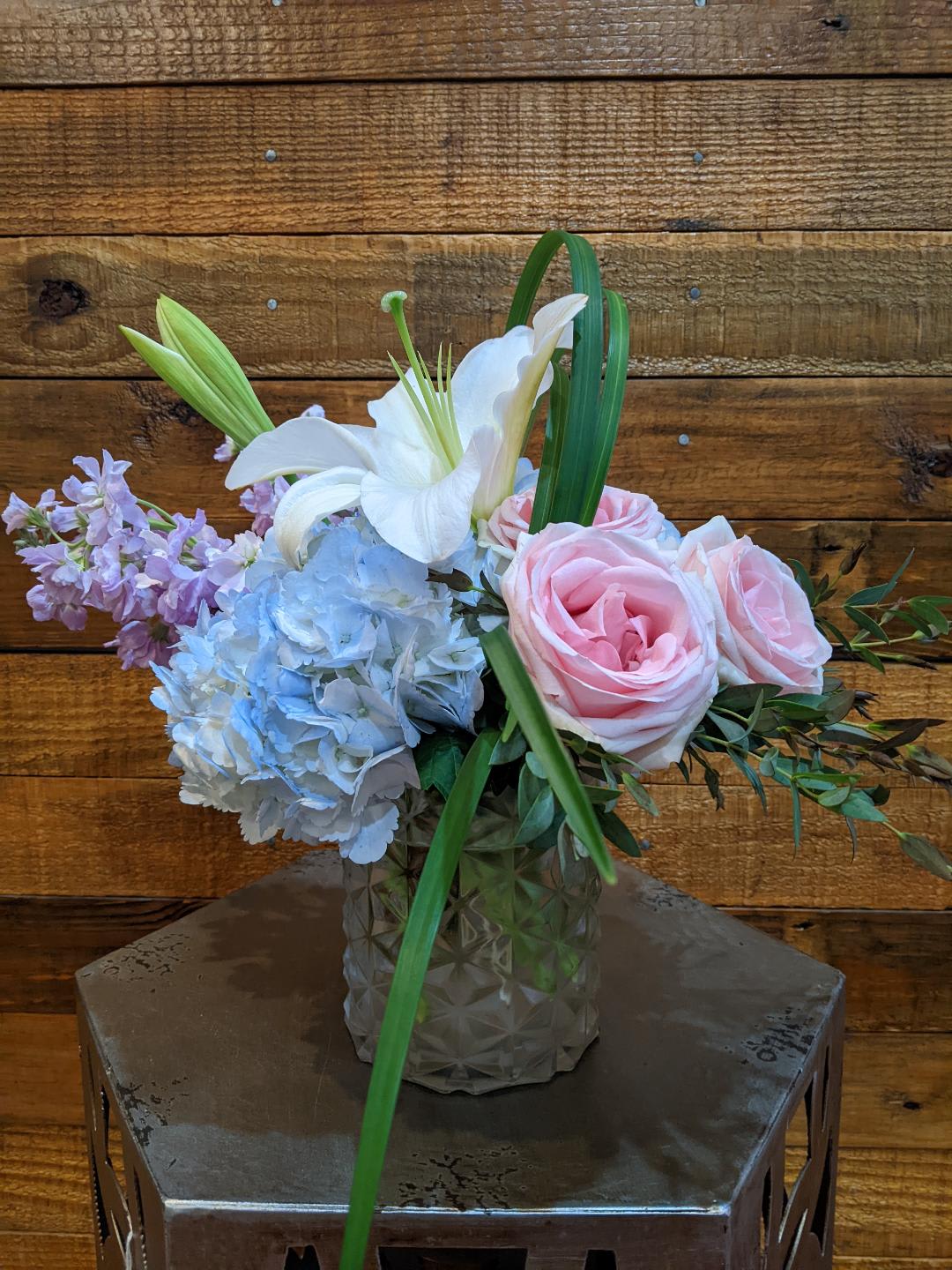 Pink roses, blue hydrangea, and a white lily in a glass vase