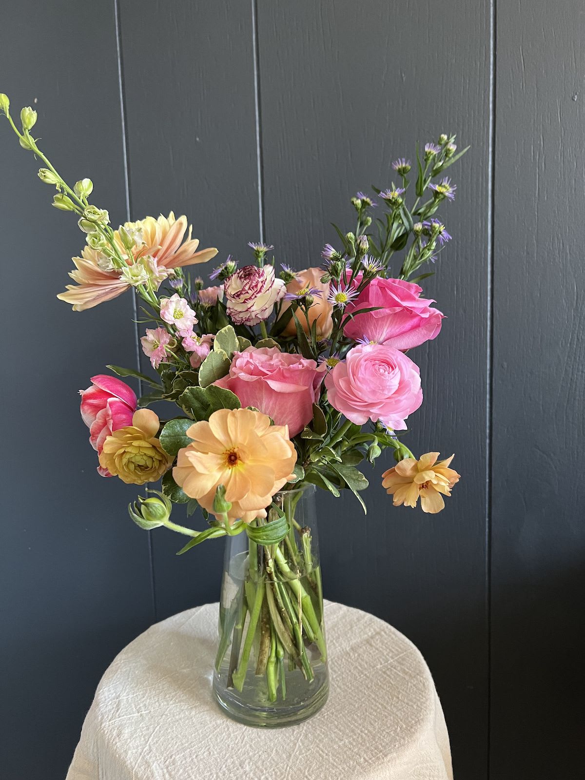 PETITE SEASONAL ARRANGEMENT IN GLASS VASE, DESIGNER'S CHOICE - Seasonal, colorful flowers and foliage artfully arranged in a clear glass vase.  Year round flowers that we typically stock: specialty rose, spray rose and garden rose, ranunculus, anemone, gerbera daisy, protea, lisianthus, chrysanthemum, larkspur, snapdragon, delphinium, stock, aster, dianthus, hypericum, feverfew, astrantia, leucodendron.