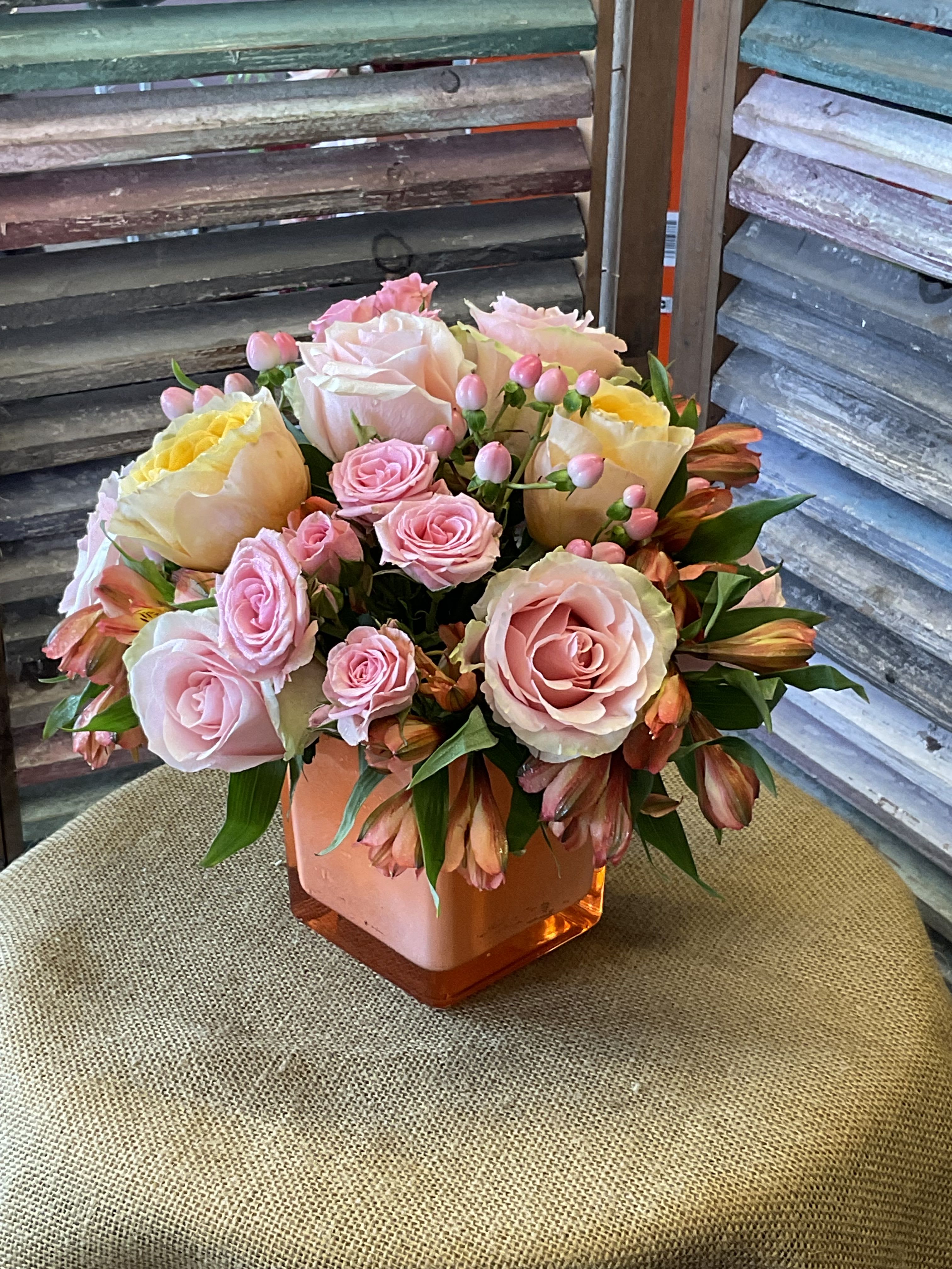 26-124 - Soft yellow garden roses and pale pink roses with spray roses and orange alstroemeria in a square glass vase.