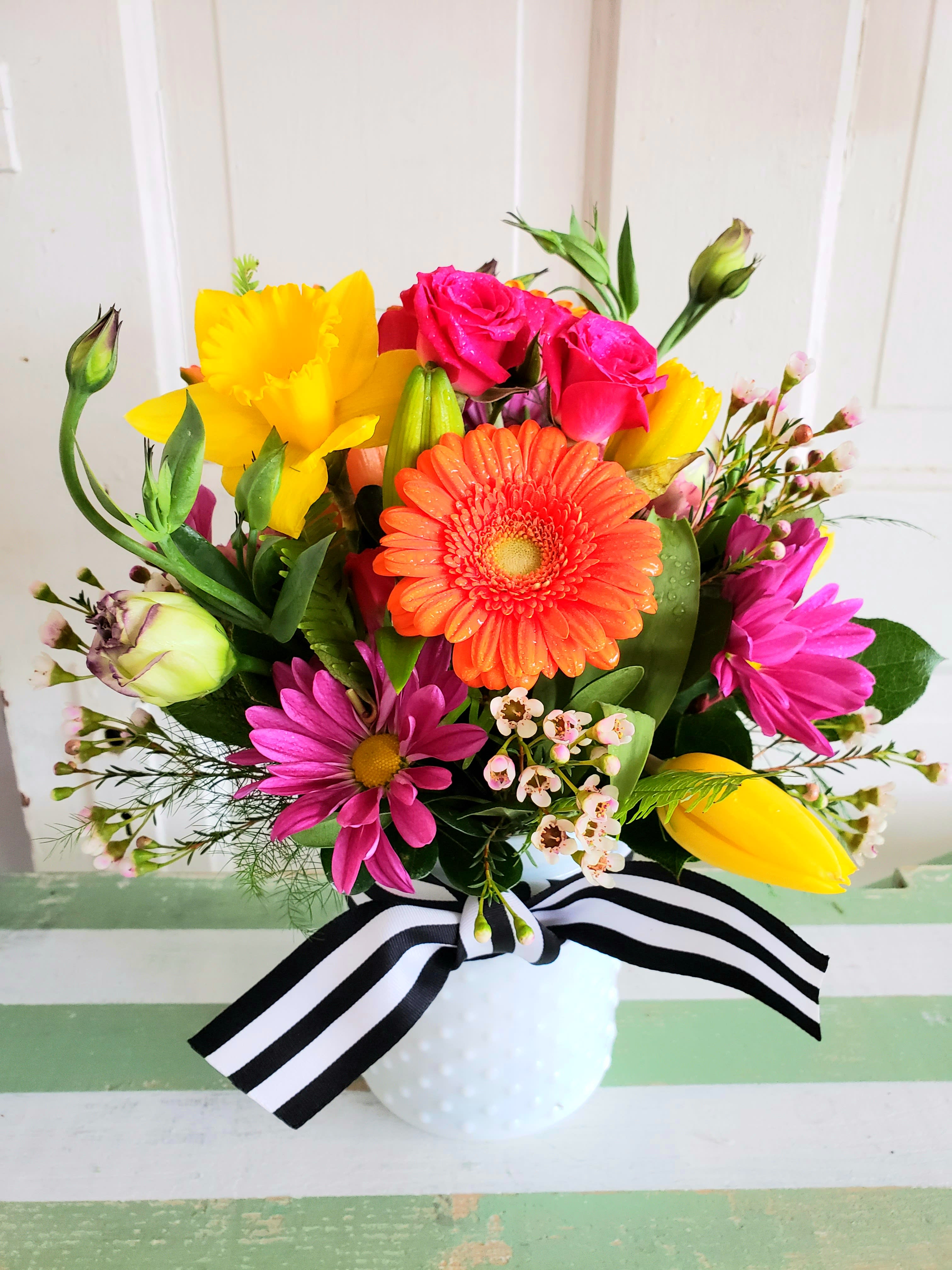 Bright mixed bouquet in a white vase with a black-and-white ribbon