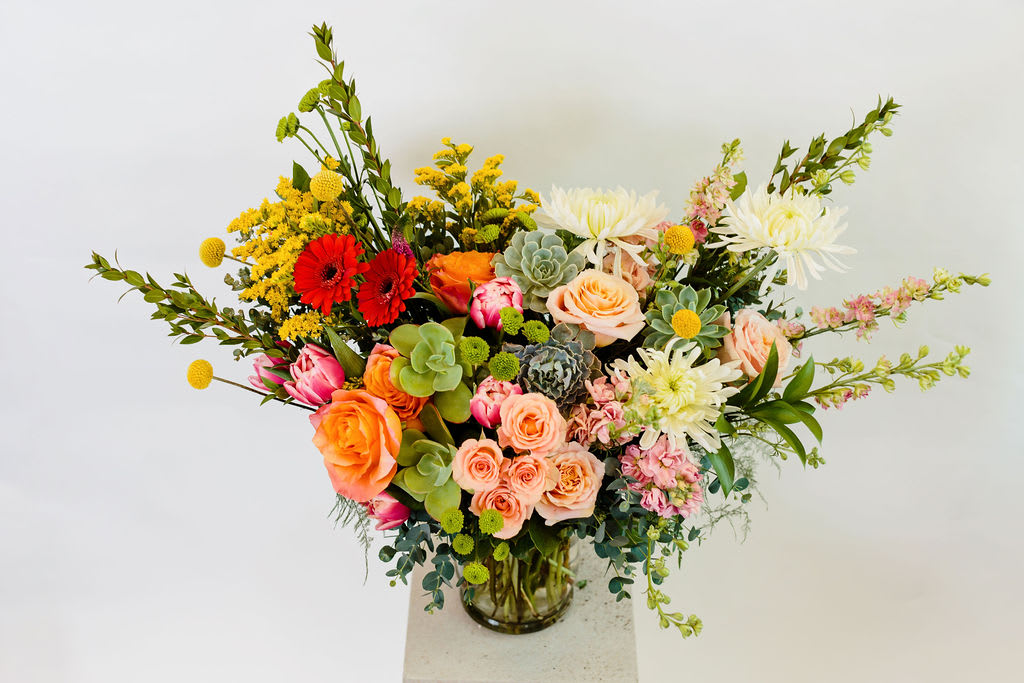 Mixed bouquet of roses, gerbera daisies, and succulents in a glass vase