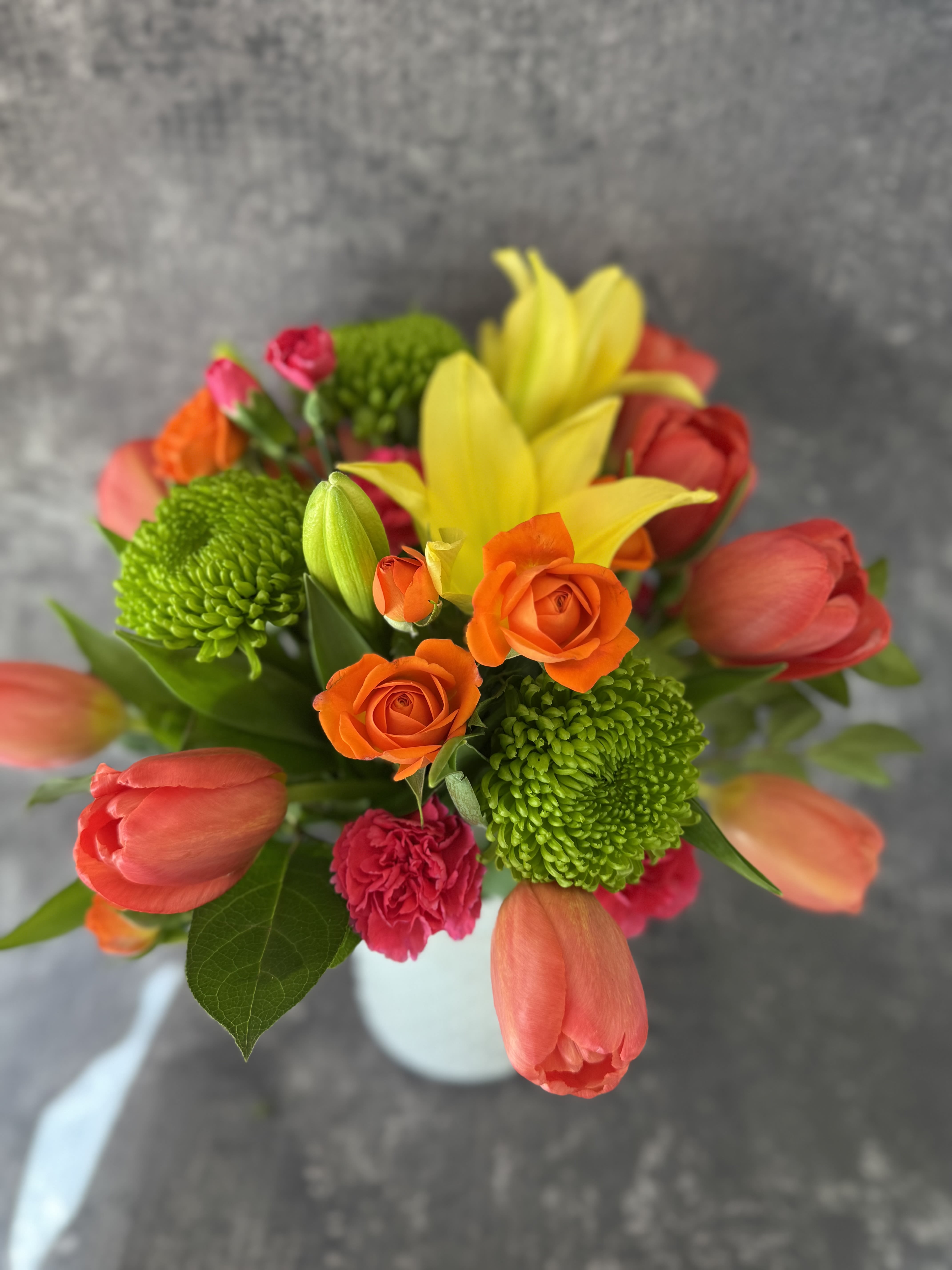Bouquet of orange roses, yellow lilies, and pink tulips in a white vase