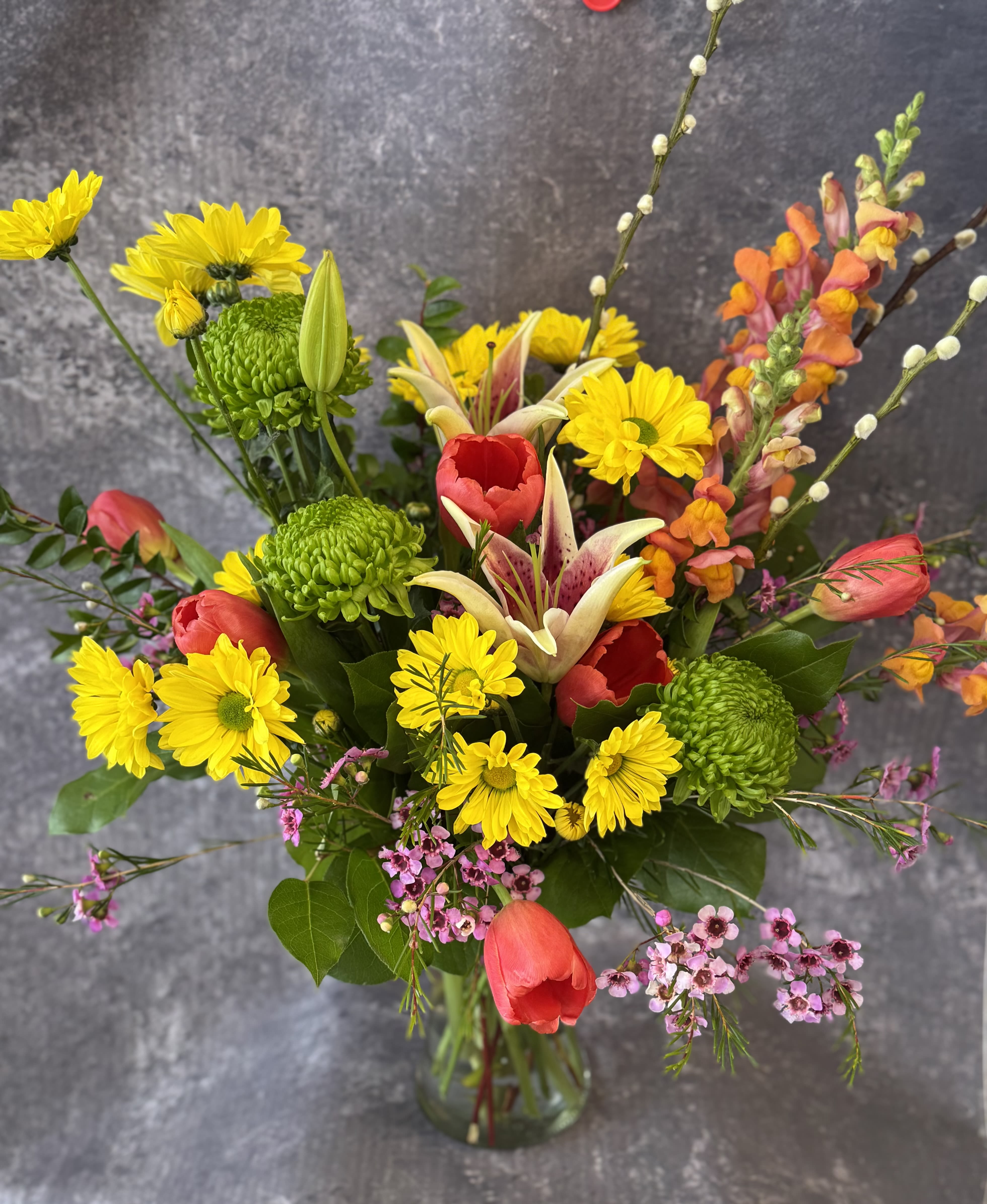Mixed bouquet of yellow daisies, red tulips, and lilies in a glass vase